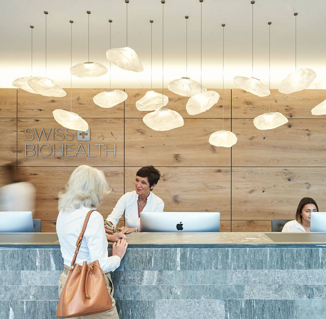 A group of runners in athletic gear race along a city street during a marathon, surrounded by spectators. Tall buildings and trees line the street, and the atmosphere is lively and energetic.